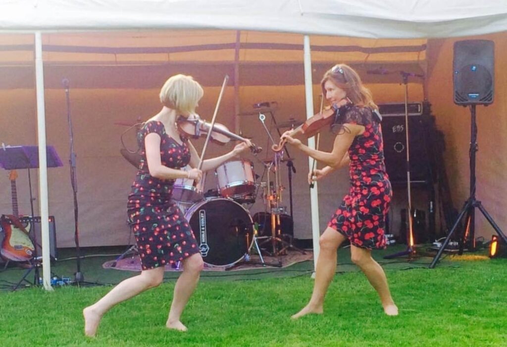 The two performers dance barefoot on the grass while playing the fiddle